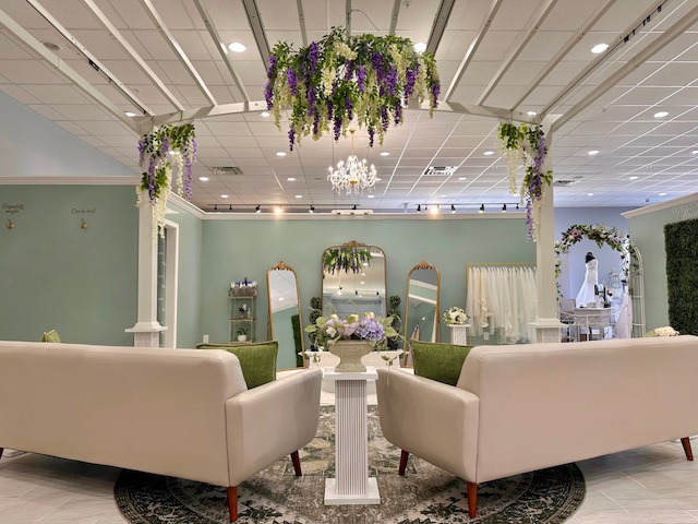 Elegant event space with floral decorations, mirrors, and sofas arranged around a central table, with a chandelier overhead.