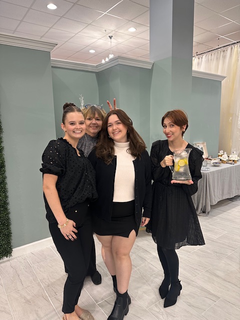 Four women standing together indoors, dressed in formal attire, posing for a photo.