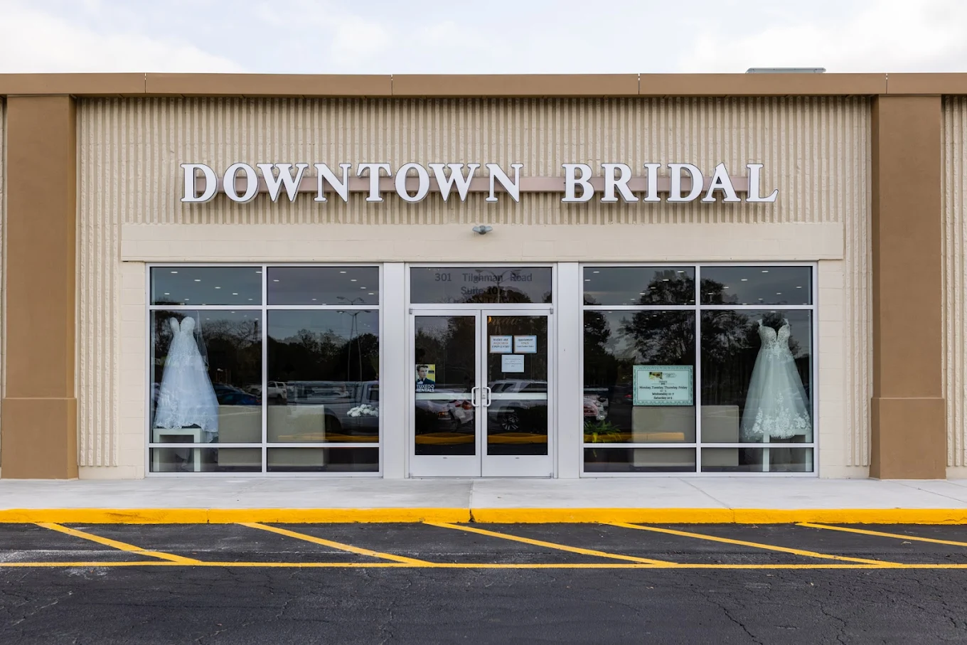 Storefront with large glass windows and doors, sign reads 'DOWNTOWN BRIDAL', two mannequins in wedding dresses inside.