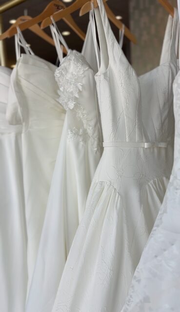 Several white dresses hanging on wooden hangers, displayed in a row.