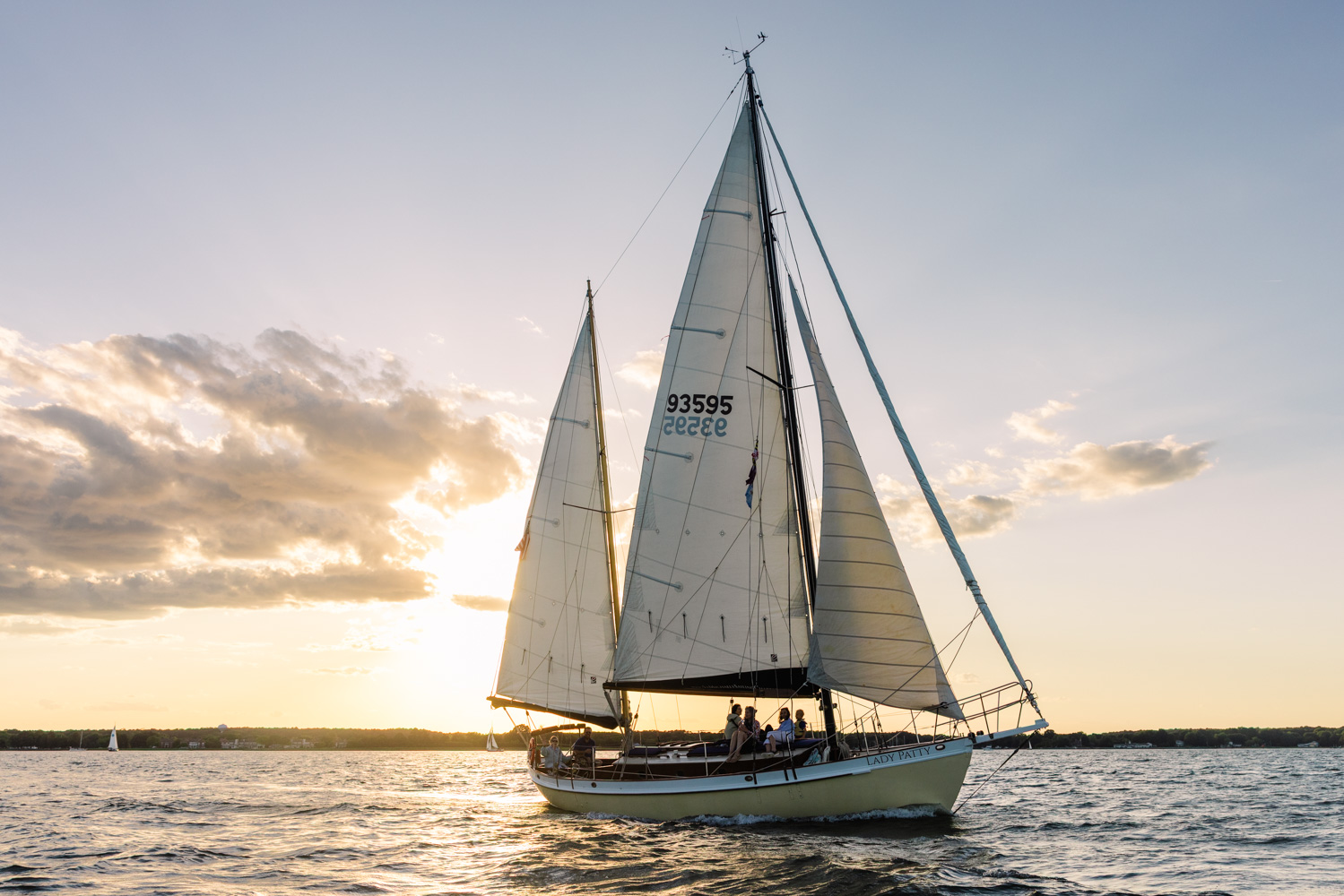 Sailboat with large sails on water during sunset, clouds in sky, horizon in background.