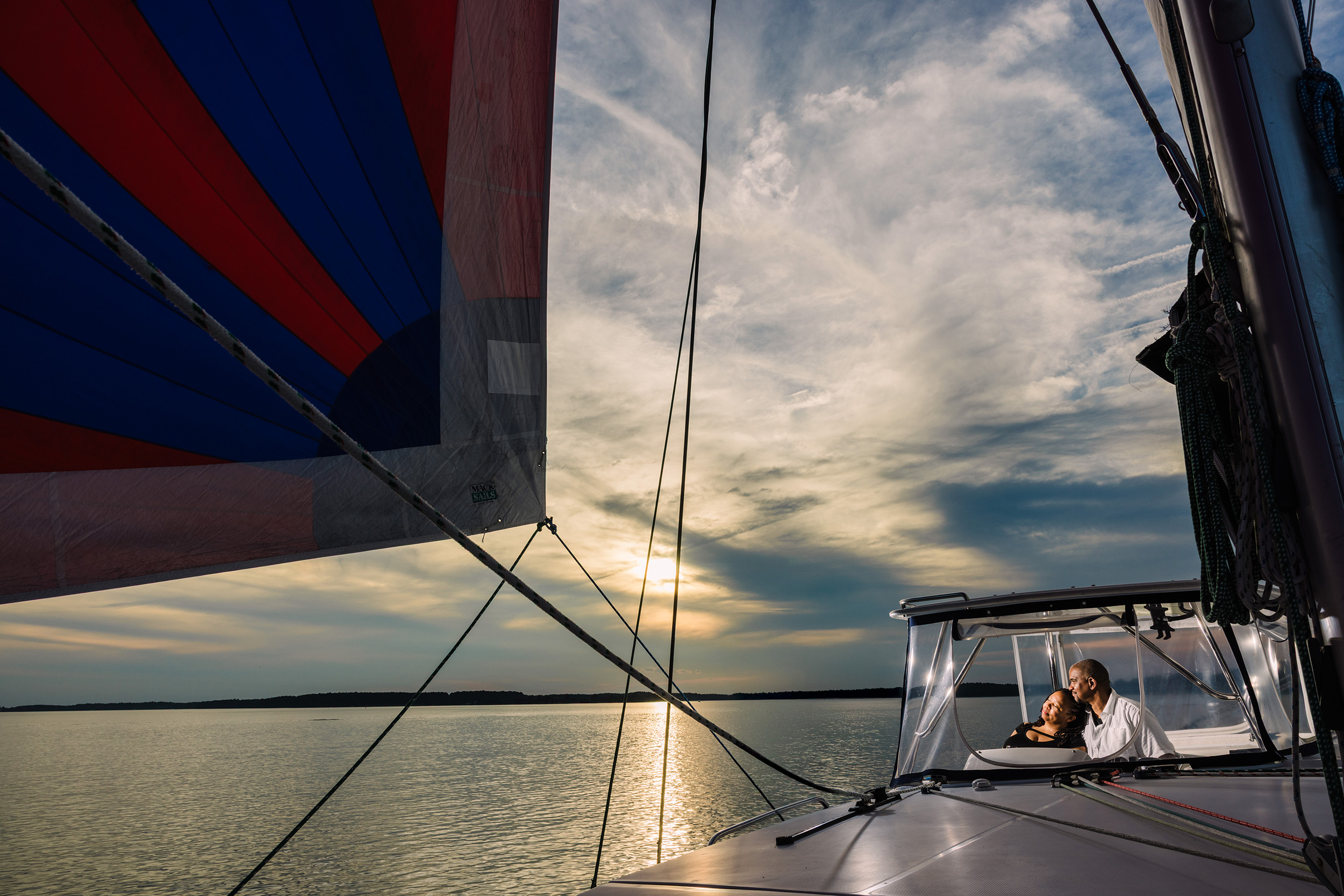 View from a sailboat showing the sky, water, and a person sitting under a canopy, with sails and rigging visible.
