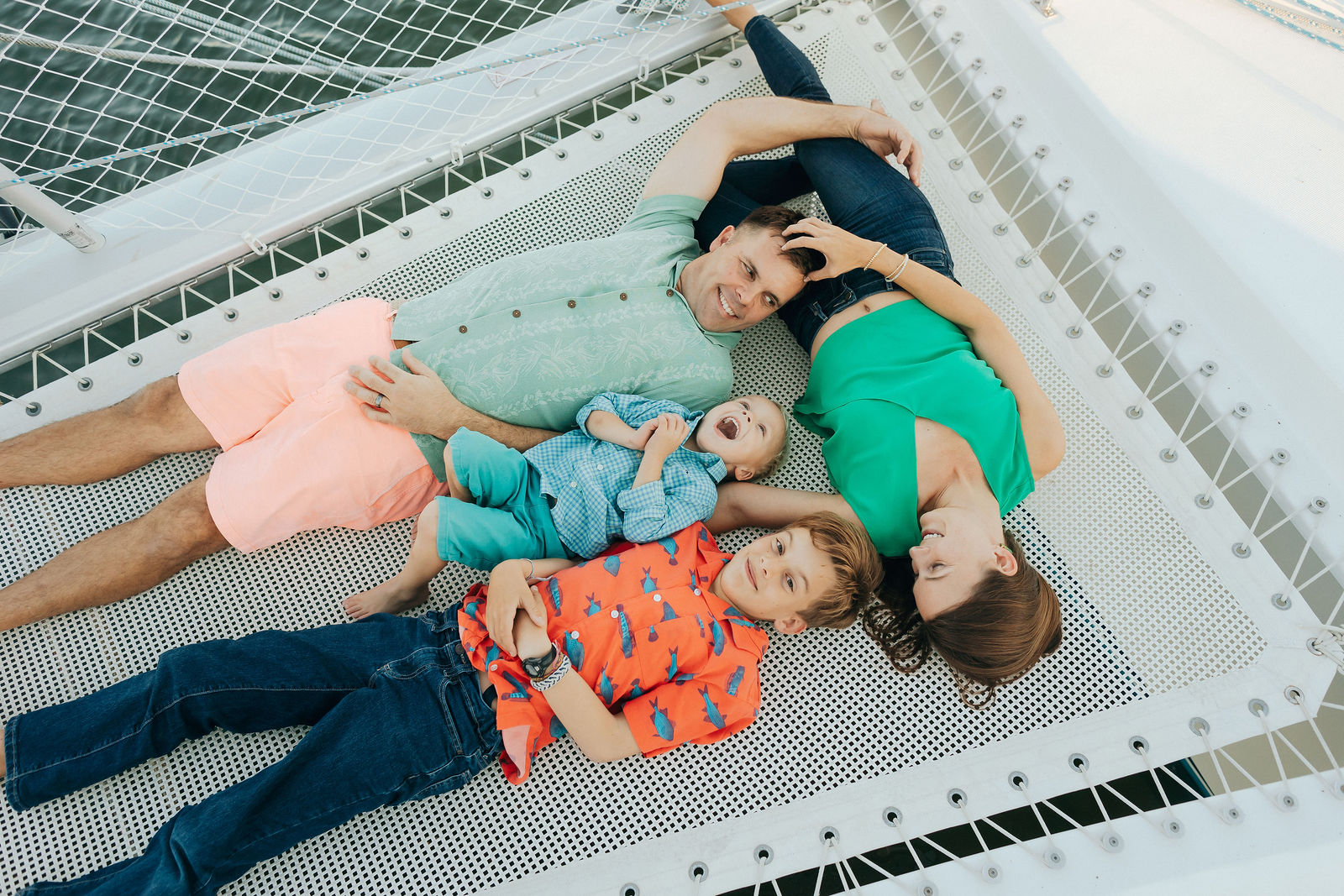 Four children lying on a mesh surface, with two girls and two boys, smiling and looking at the camera.