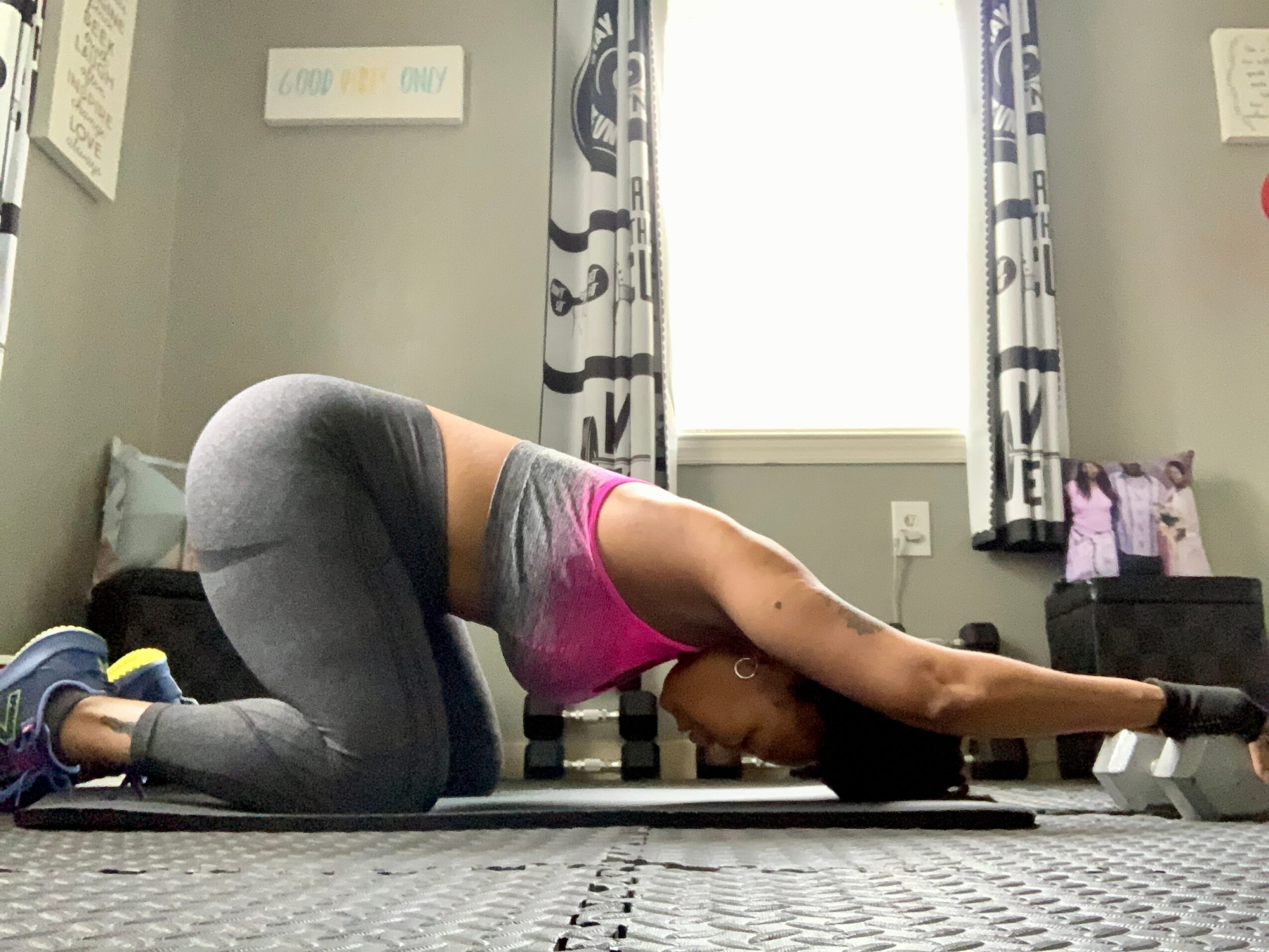 Person practicing yoga in child's pose on a mat in a room with curtains and wall decorations.