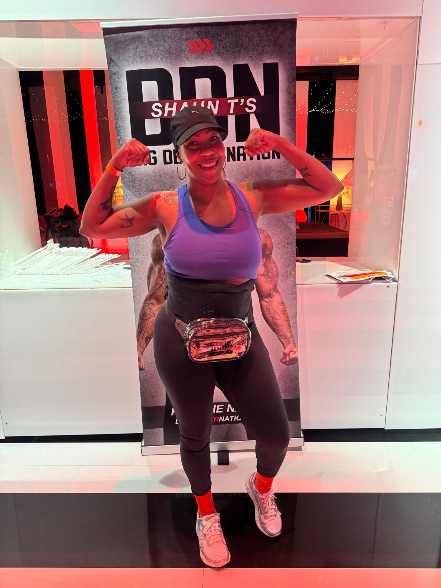 Woman standing in front of a sign, wearing athletic clothing and a waist bag, with a modern interior background.