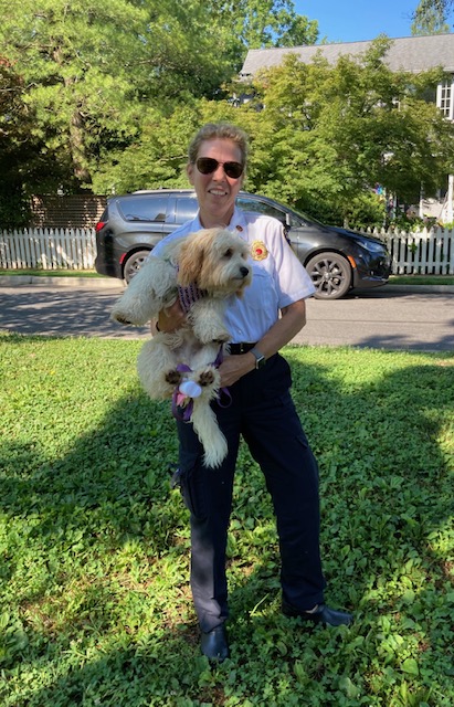 Person holding a fluffy dog outdoors on grass, with trees, a house, and a parked car in the background.