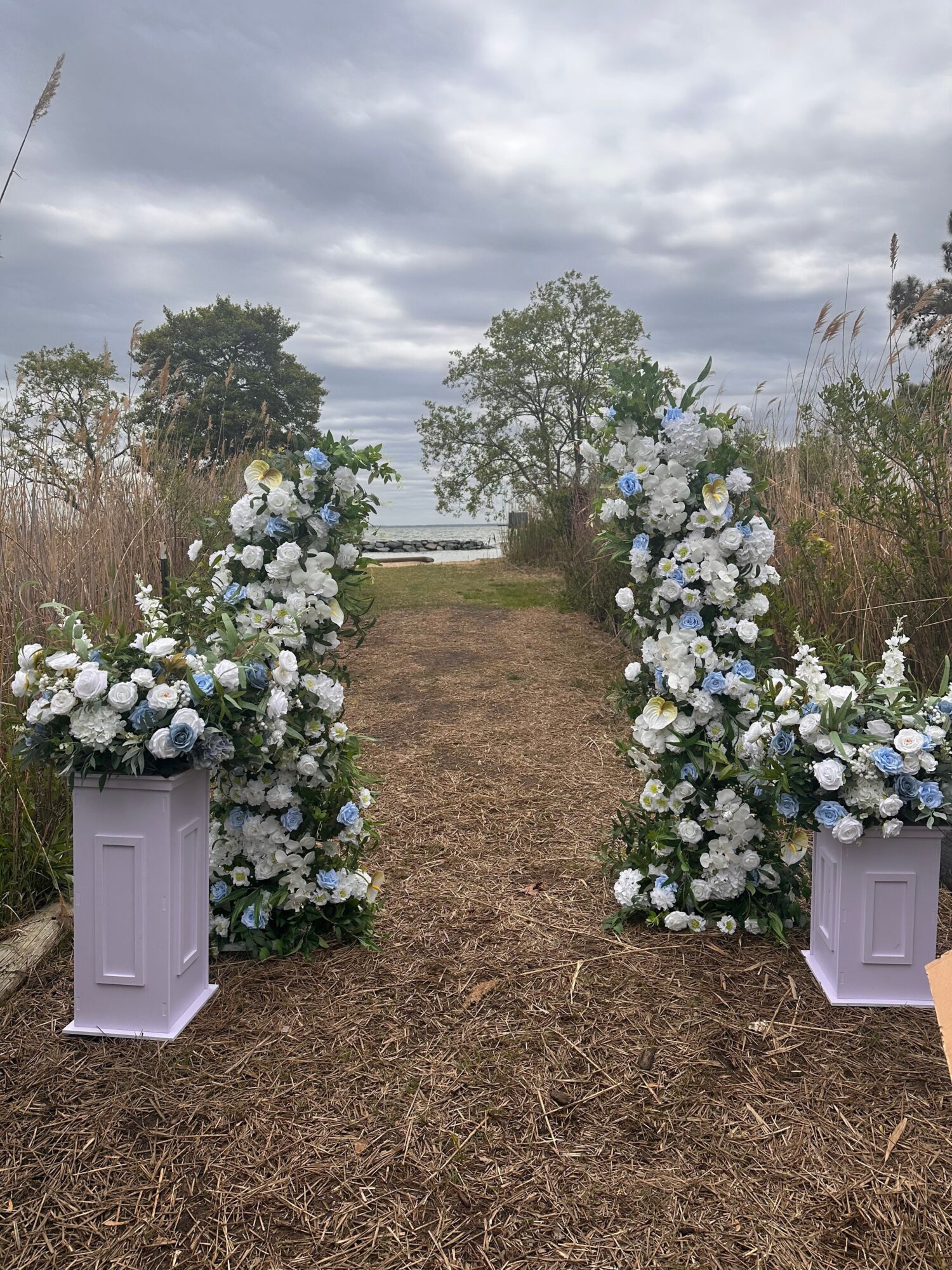Outdoor scene with floral arrangements and white doors on a grassy area under cloudy sky.