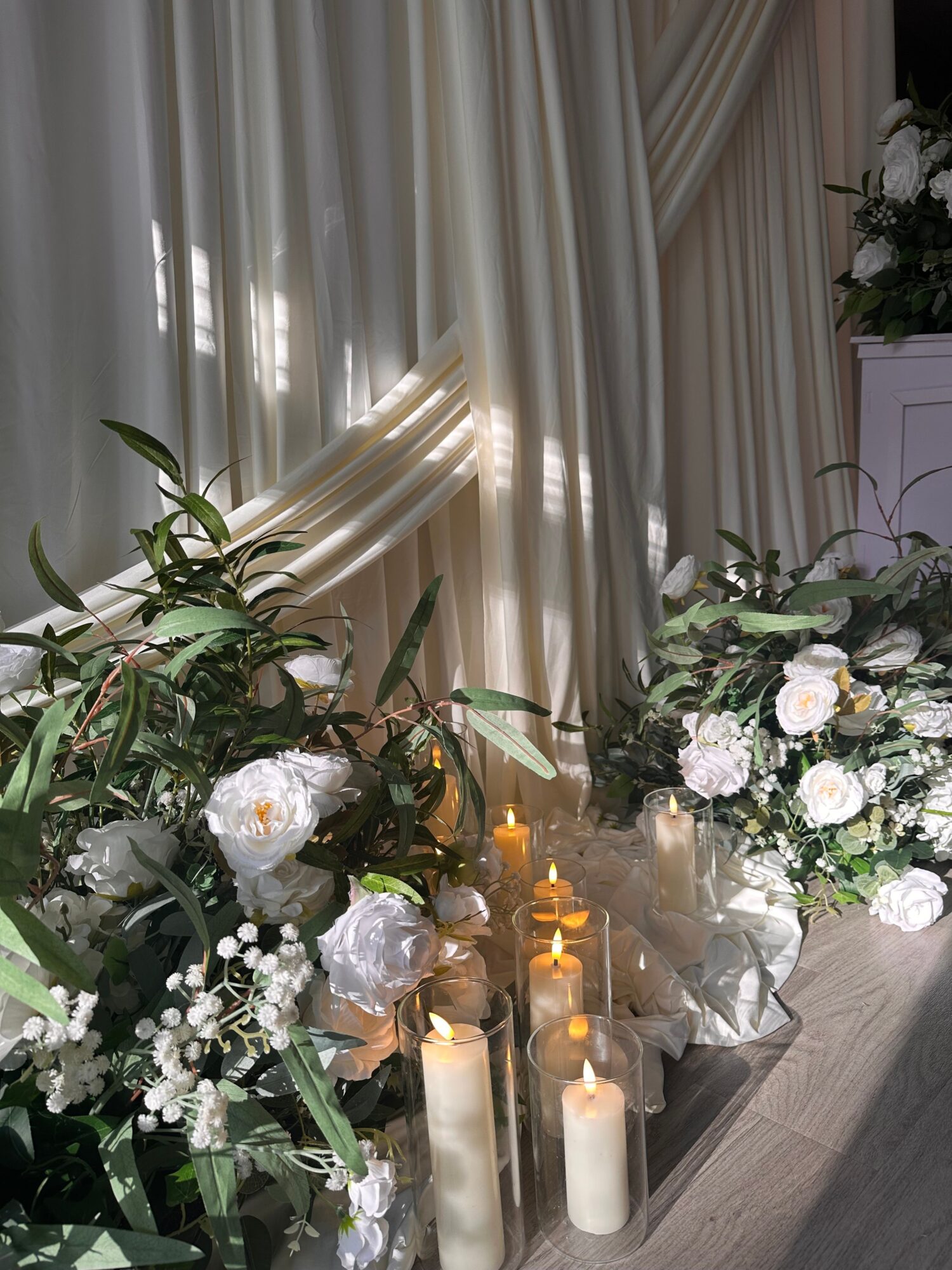 Floral arrangement with white flowers, candles, and greenery on a table, viewed from the side.