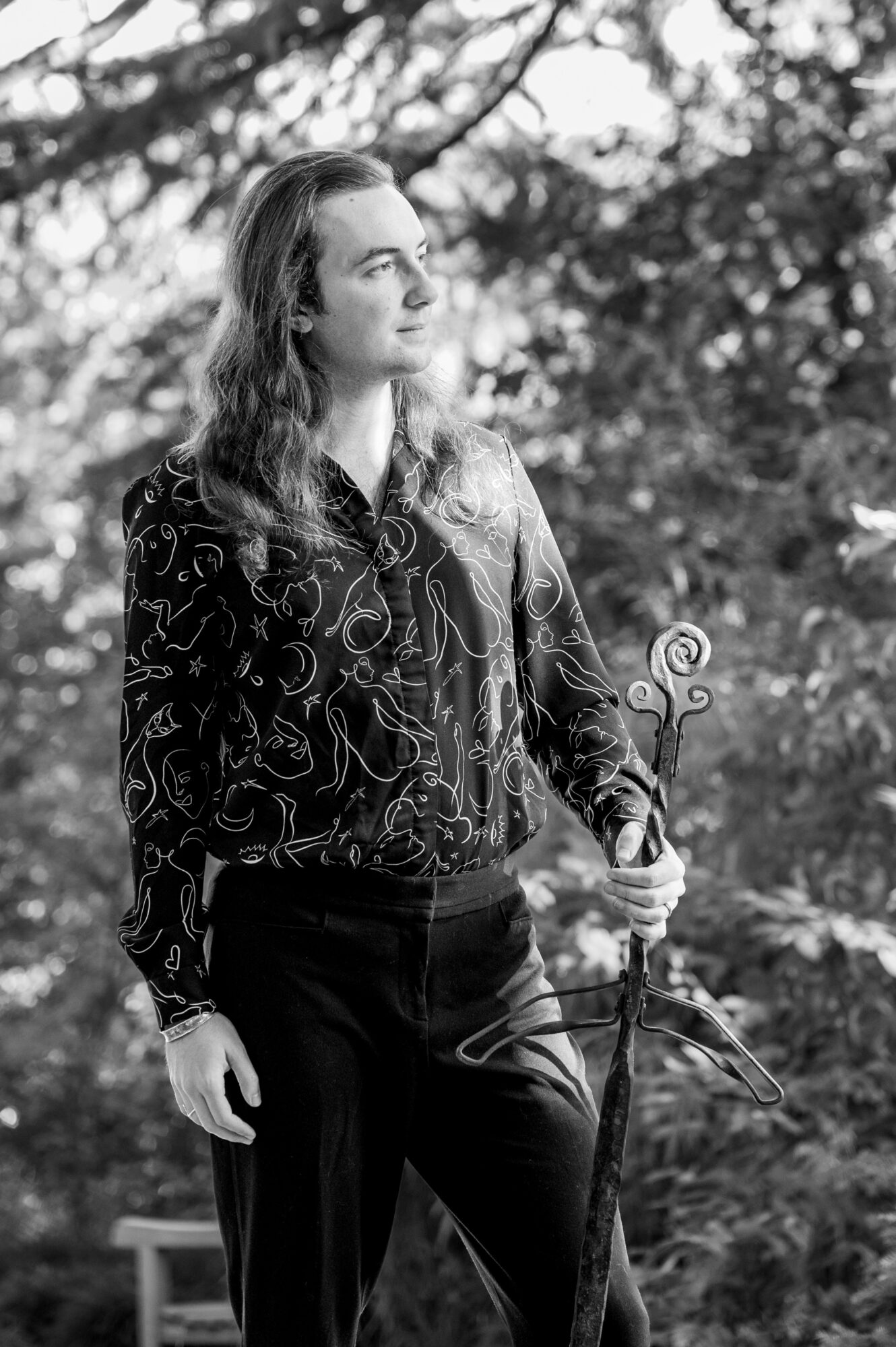 Woman with long hair holding a decorative plant in an outdoor setting, trees in the background.