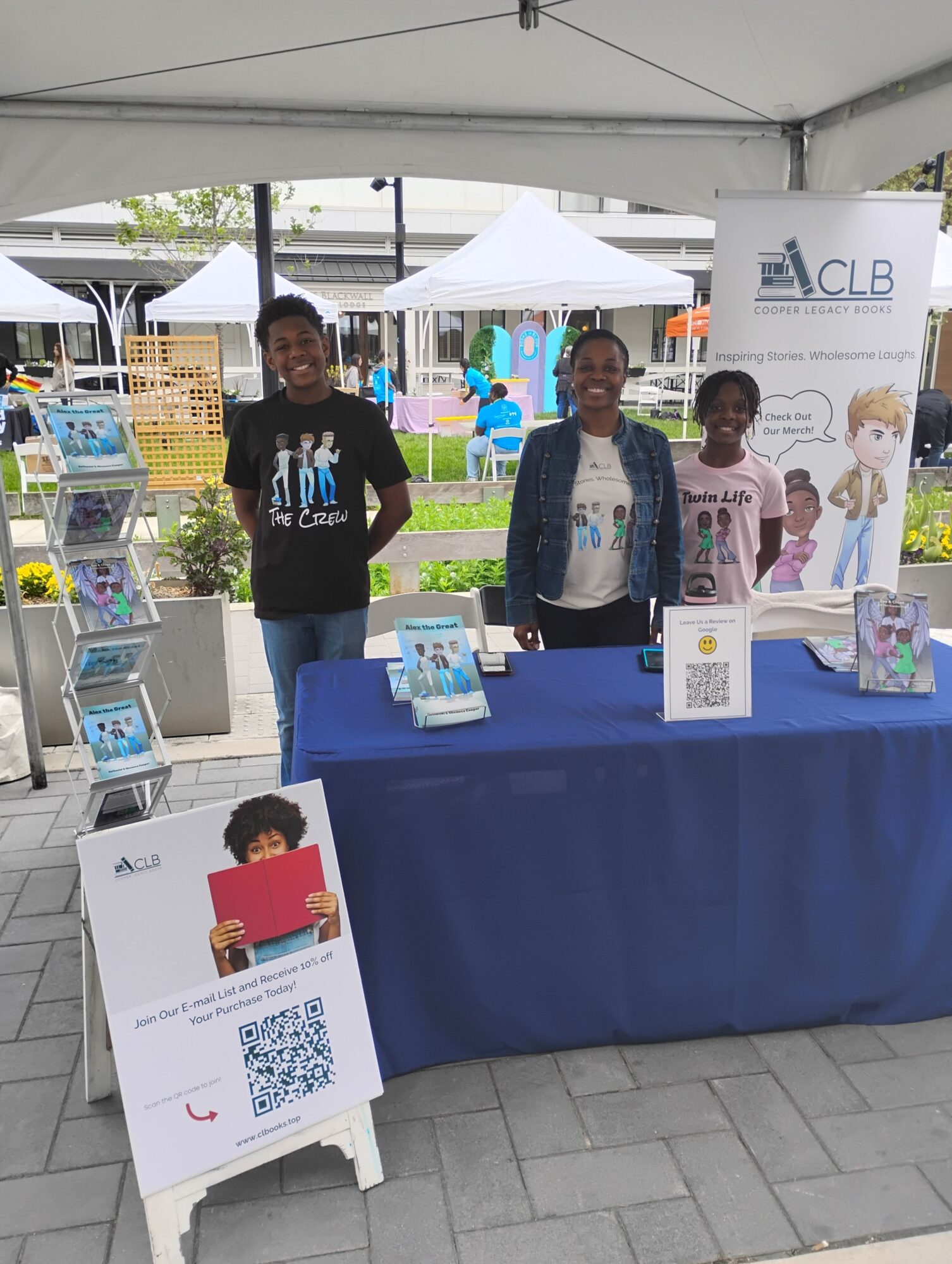Three people standing behind a table with promotional materials at an outdoor event, with a QR code sign in front.