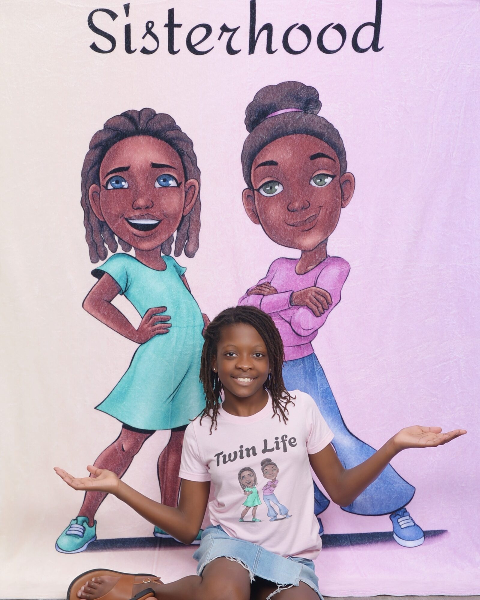 Girl with long hair smiling, wearing a white shirt with twin girls, standing in front of a sisterhood mural.