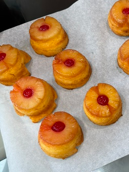 Seven pineapple upside-down cupcakes with cherries on top on parchment paper.