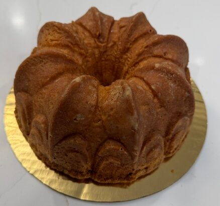 A bundt cake on a gold-colored base, with a golden-brown crust and a textured surface.