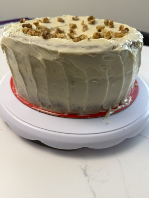 Cake with white frosting, topped with nuts, on a white plate with red sauce underneath, viewed from the side.