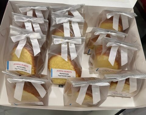 Box of individually wrapped baked goods with white ribbons, labeled as pumpkin cake and pound cake, arranged in two rows.