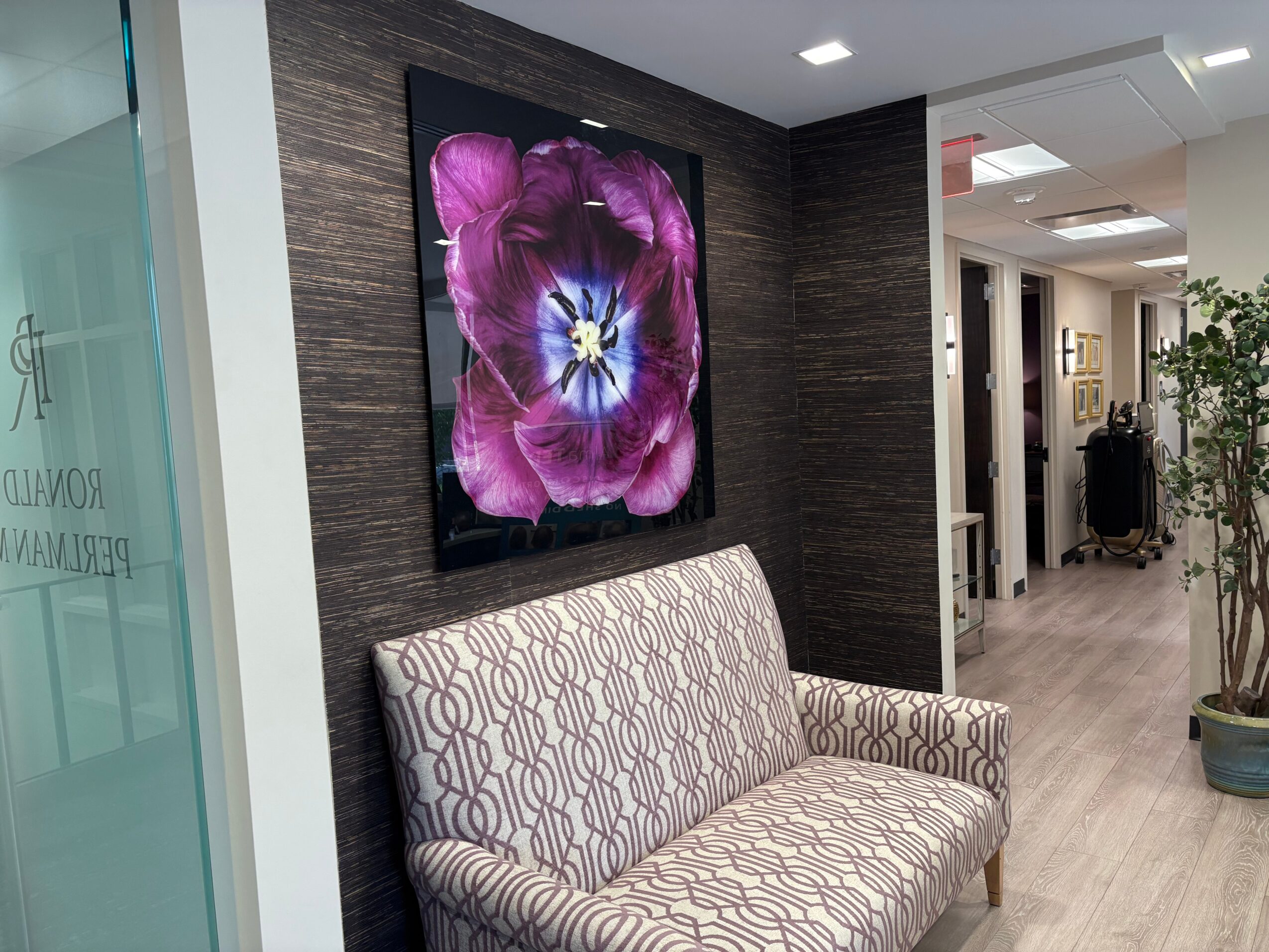 Interior of a modern room with a patterned sofa, dark textured wall, and a large floral artwork, with a hallway visible in the background.