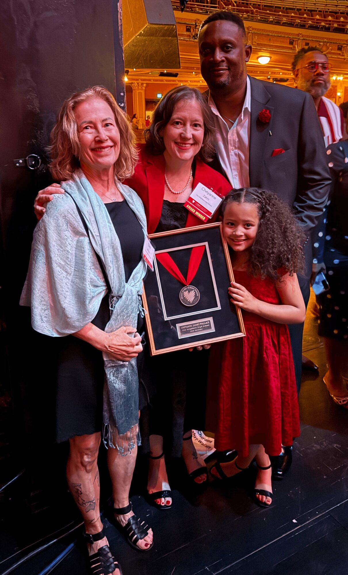 Four people, two adults and two children, smiling and holding a framed award at an indoor event.