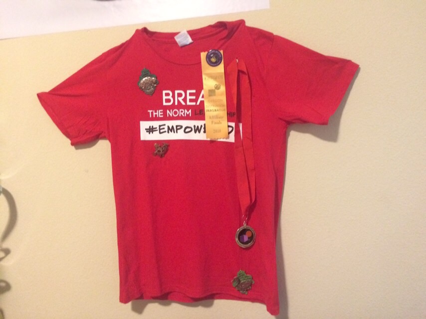 Red children's T-shirt with text and patches, hanging on a wall.