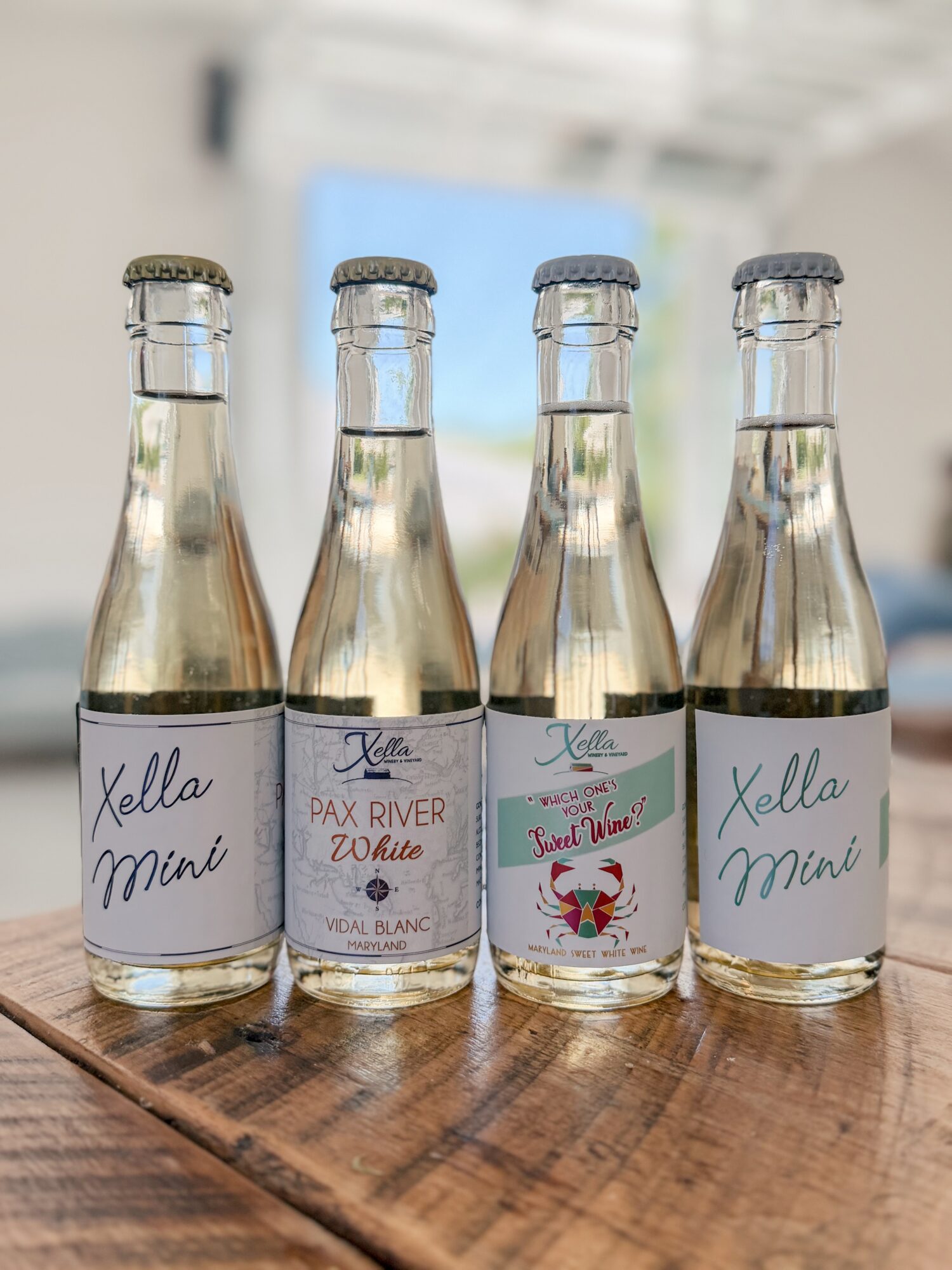 Four glass bottles with labels, placed on a wooden surface, with a blurred background.