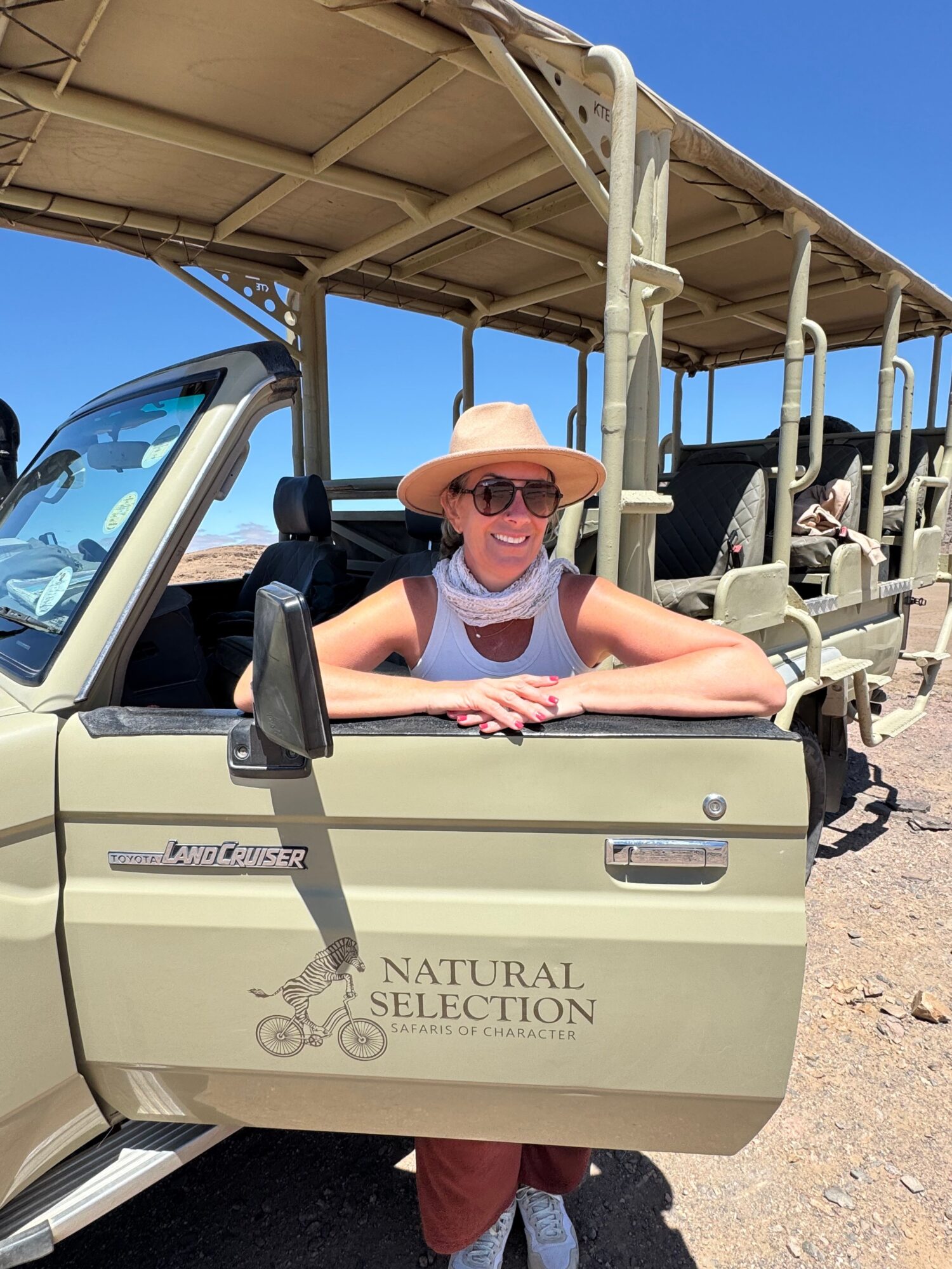 Person wearing sunglasses and a hat sitting in a golf cart outdoors, with a clear blue sky in the background.