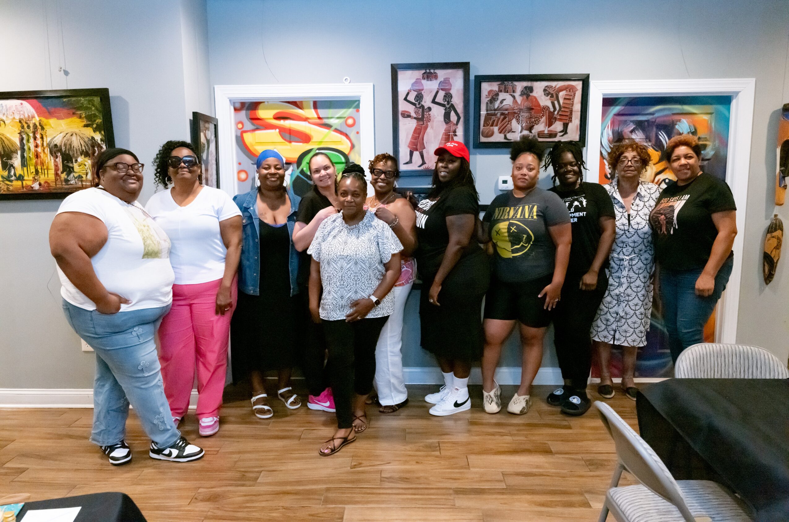 Group of people standing in an art gallery with colorful paintings on the wall, smiling and posing for the photo.
