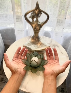 A bronze sculpture of a woman in a yoga pose on a round base, with a lotus flower-shaped object in front, on a white table.