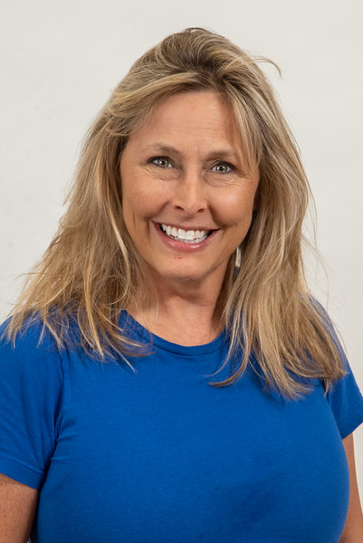 Smiling woman with blonde hair wearing a blue shirt against a plain background.