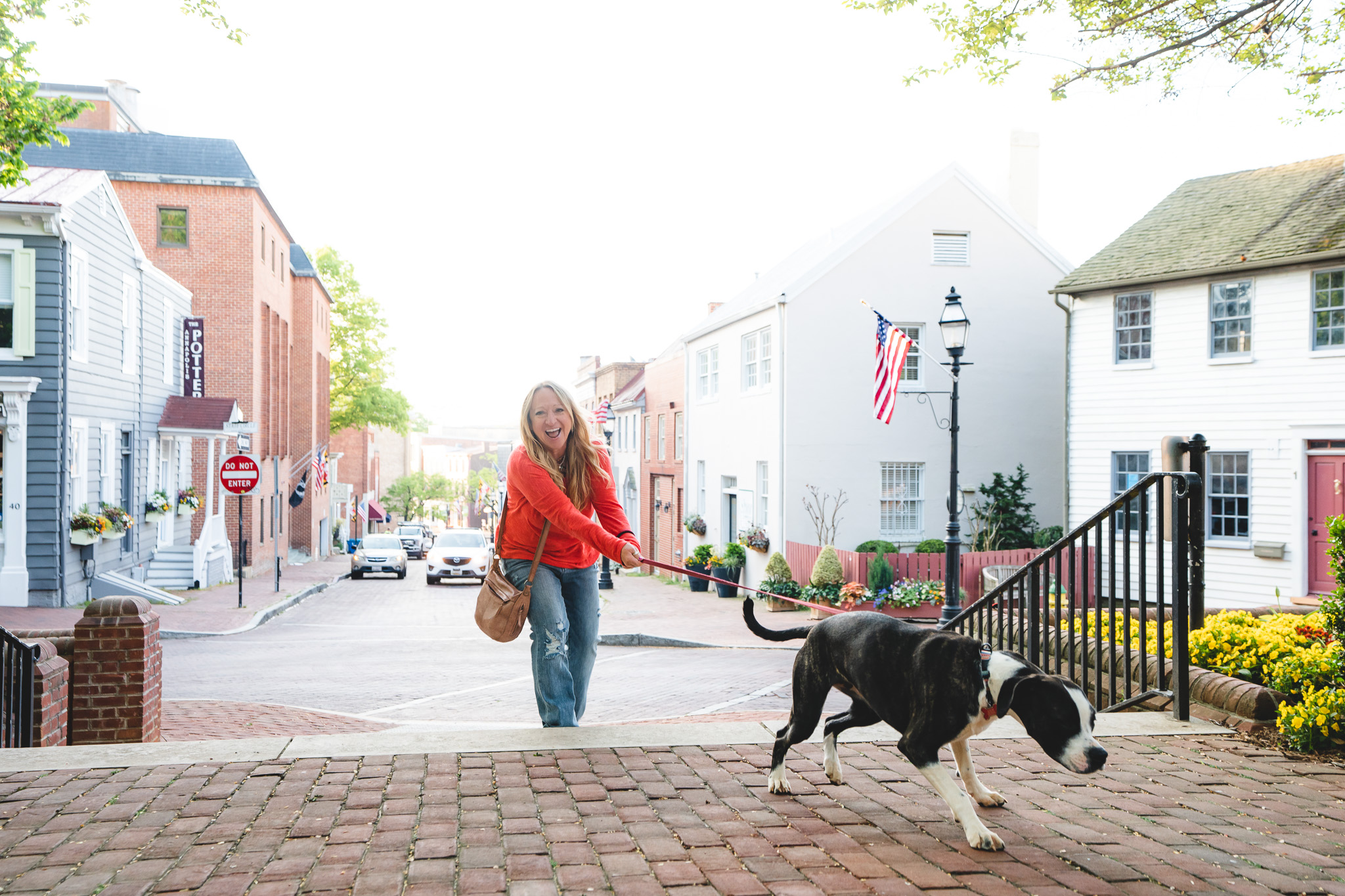 Young woman walking a black and white dog on a leash in a small town street, with colorful buildings and trees in the background.