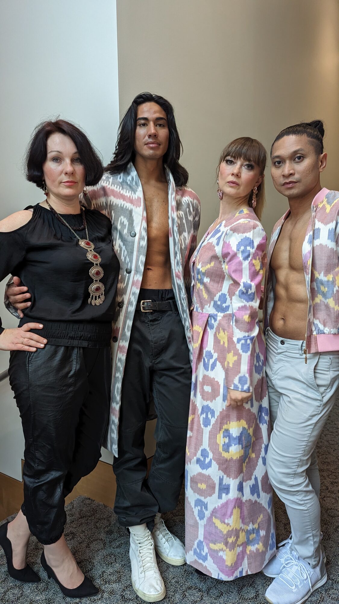 Four women standing together indoors, dressed in stylish clothing, posing for a photo.