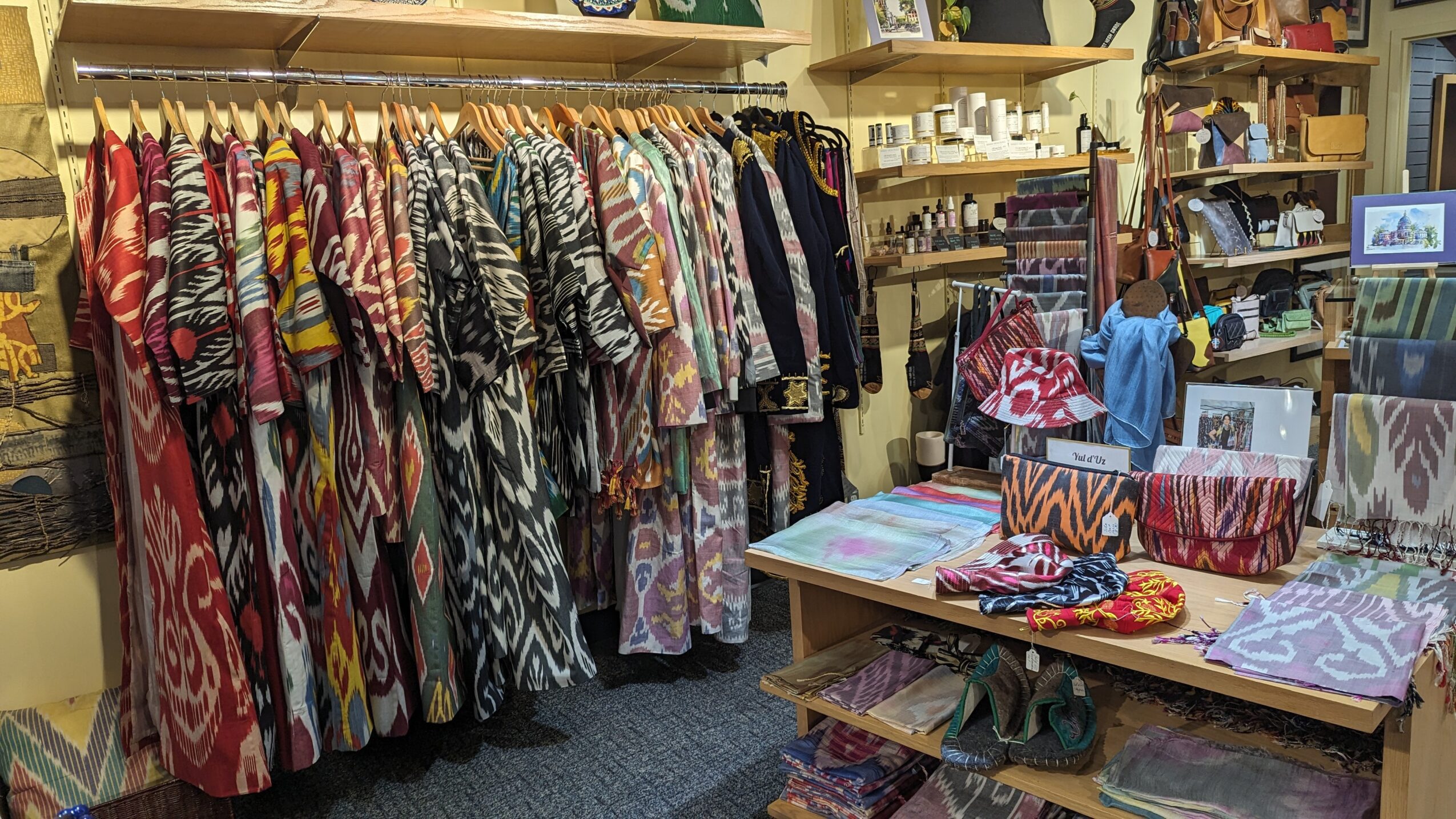 Clothing rack with colorful dresses and garments, shelves with accessories and fabric patterns, in a boutique store.