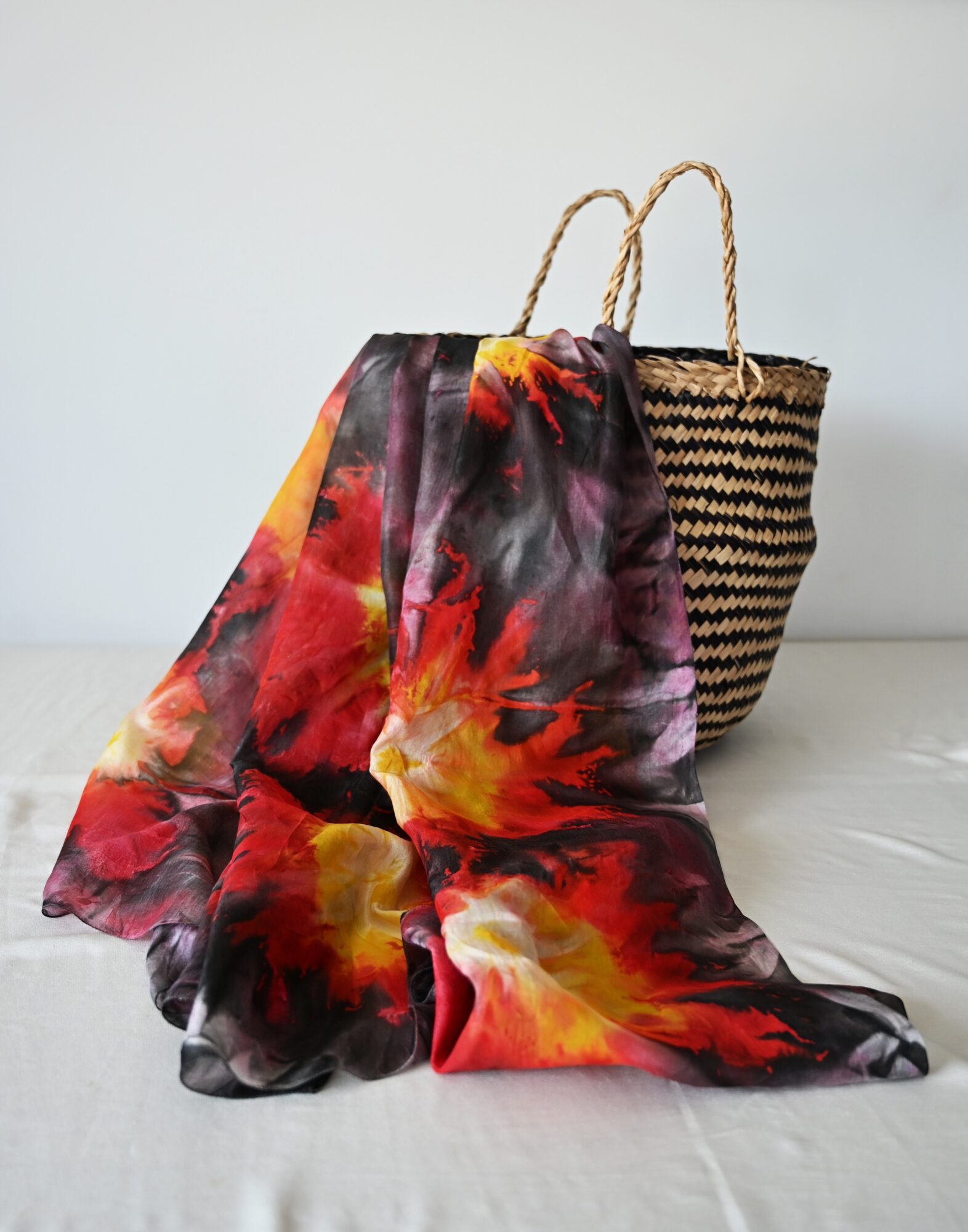Two woven bags, one with a floral scarf draped over it, on a white surface against a plain background.