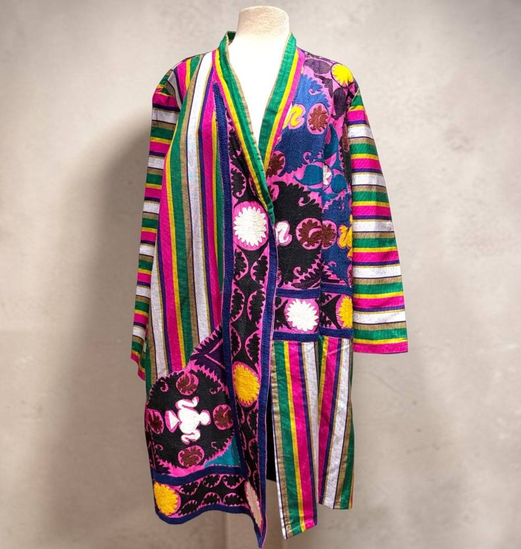 Colorful, striped and patterned coat displayed on a mannequin against a plain background.