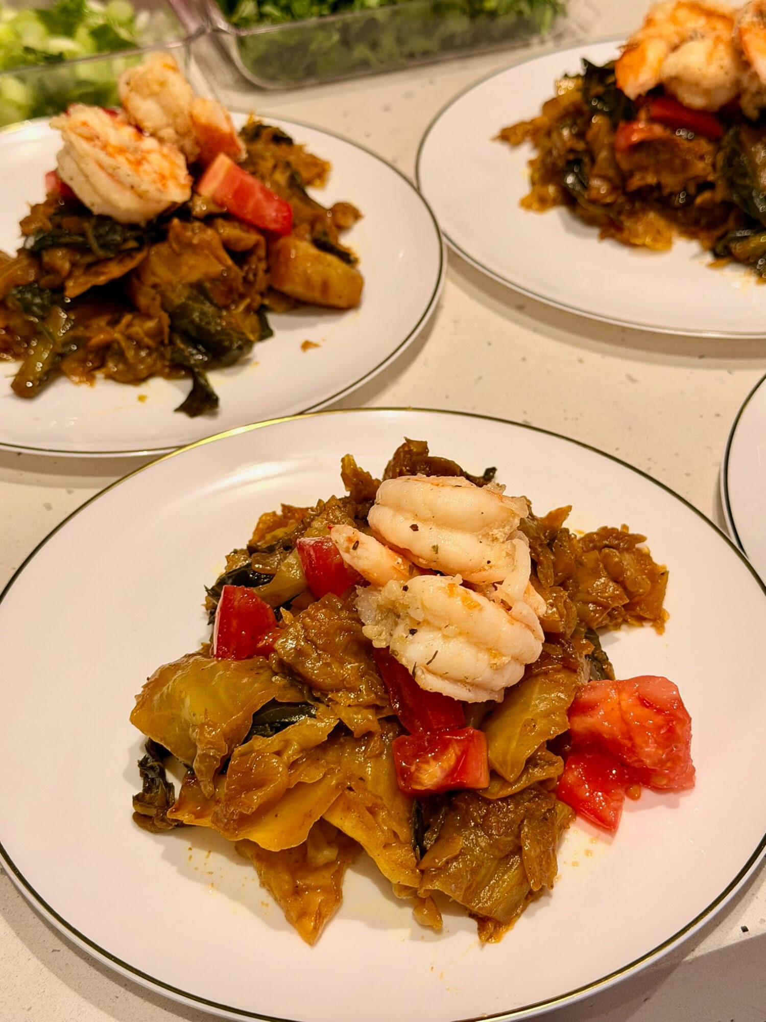 Plate with cooked greens, chopped tomatoes, and a piece of cooked fish or seafood, garnished with a lemon wedge, on a white plate.