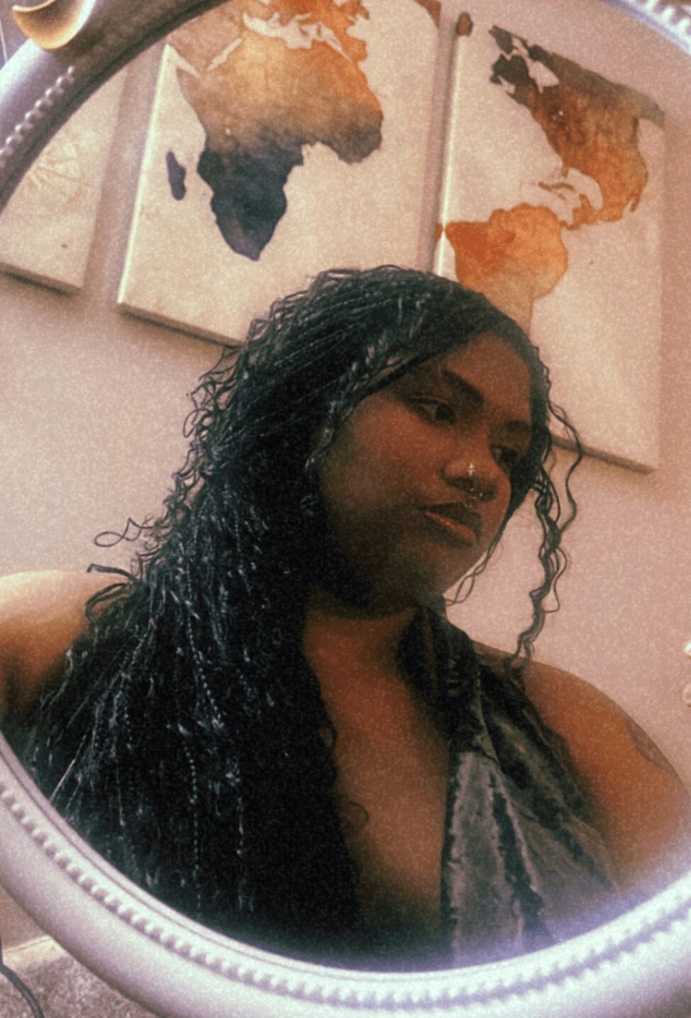 A woman with long, curly hair looking into a mirror, with world map artwork in the background.
