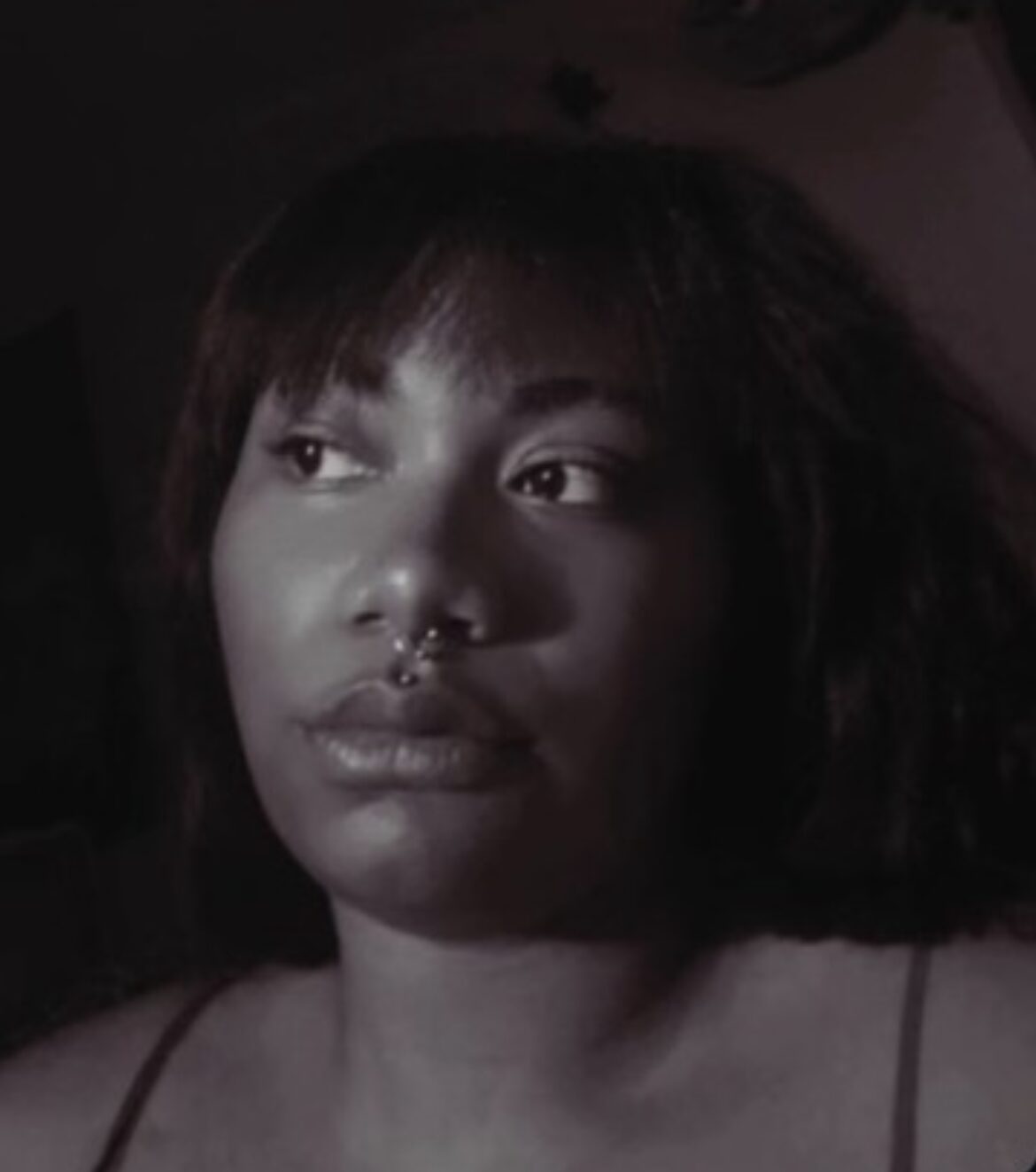 Portrait of a woman with short hair and a nose piercing, looking to the side, in black and white.