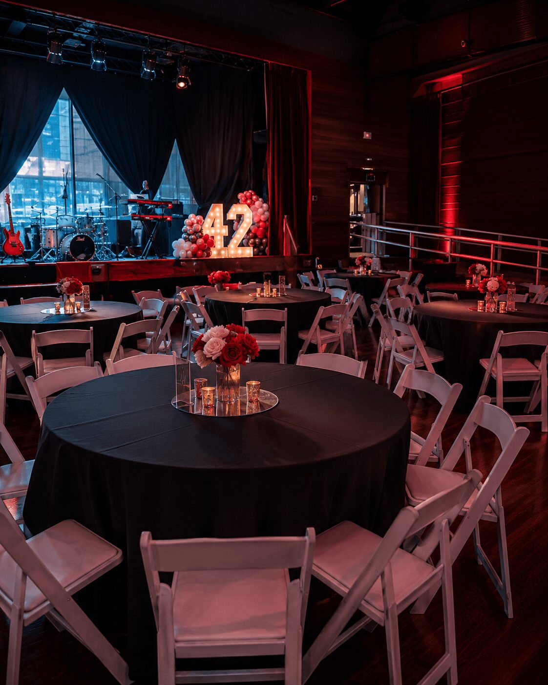 Event venue with round tables, chairs, stage with musical instruments, and a large illuminated number 12, dim lighting.