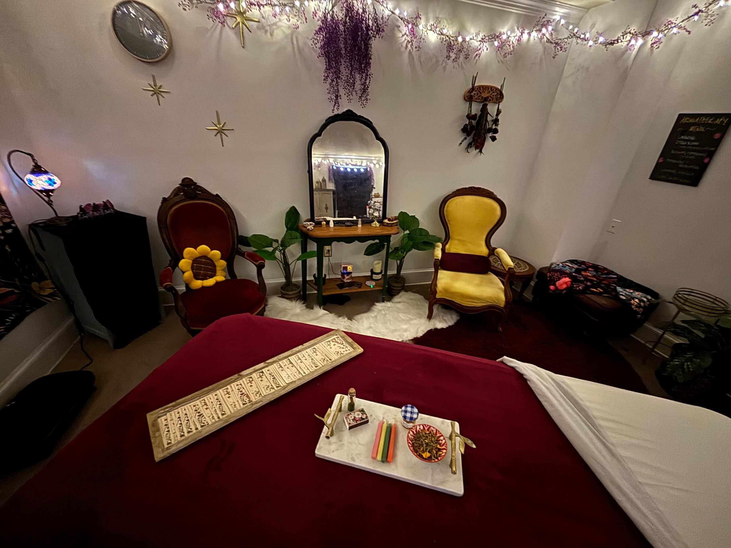 Room decorated with string lights, hanging flowers, and wall ornaments, featuring chairs, a mirror, and a table with items.