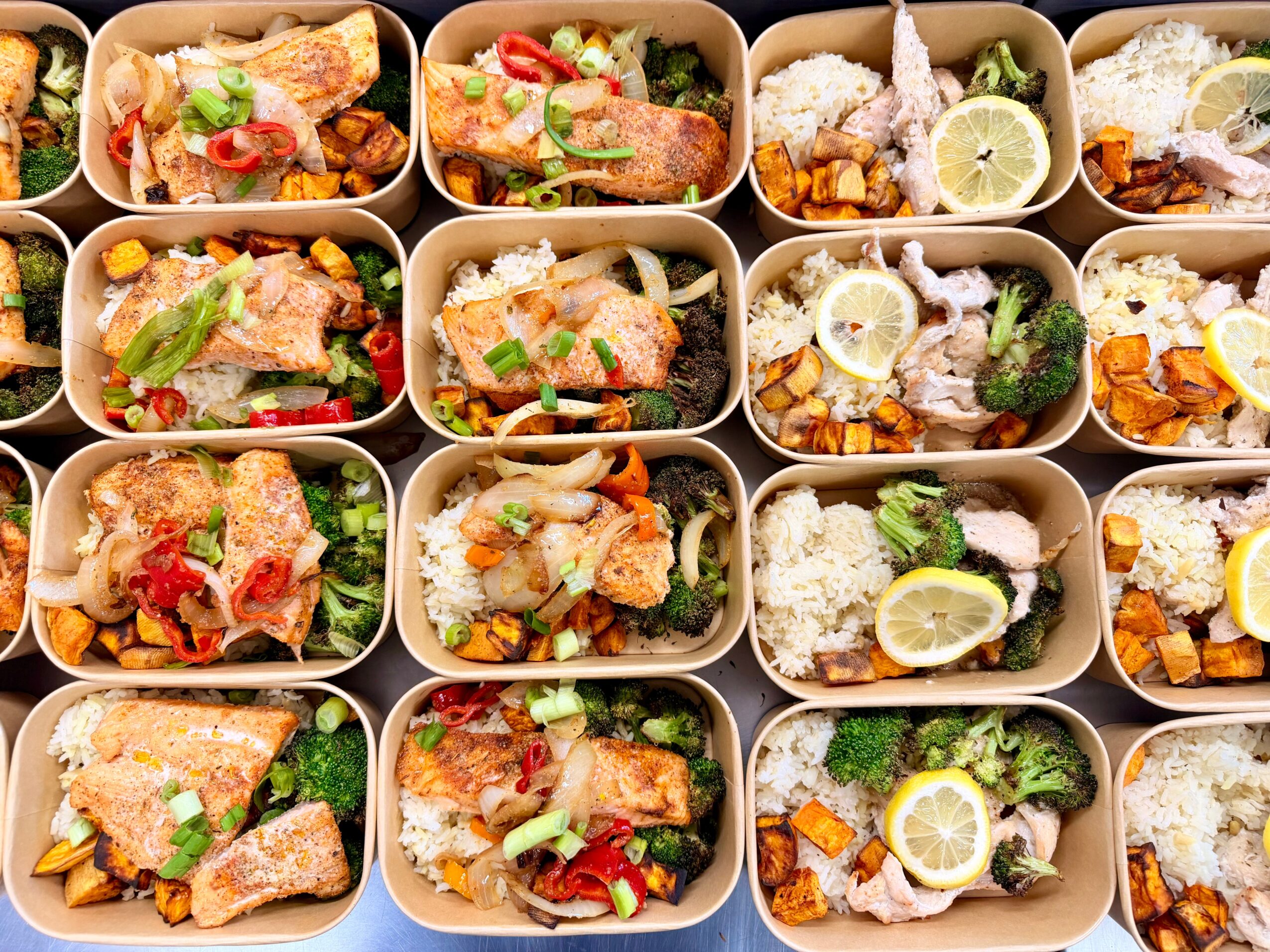 Multiple bento boxes filled with fried chicken, rice, vegetables, and lemon slices, arranged in rows.