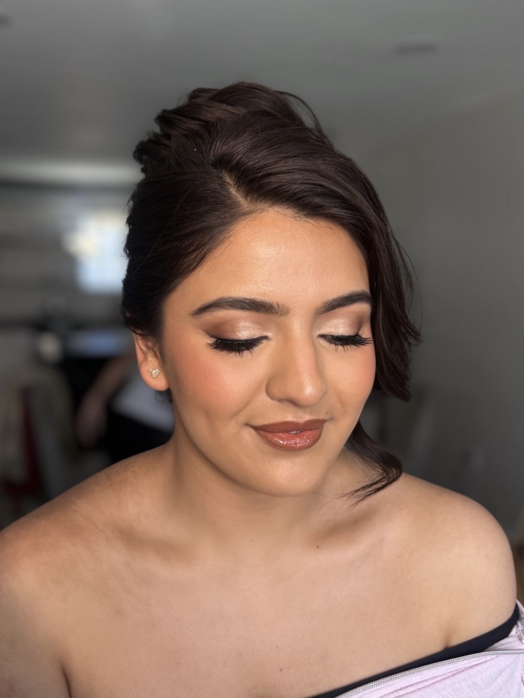 Woman with styled hair and makeup, eyes closed, smiling softly, wearing an off-shoulder top.