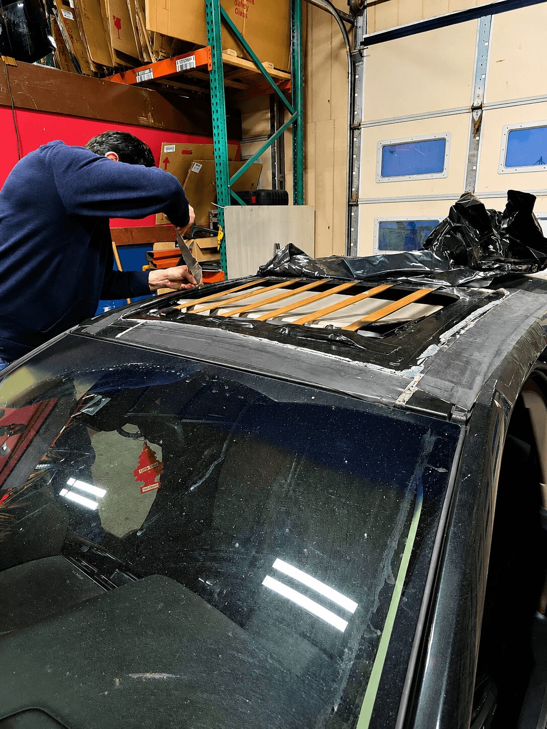 Person working on a car in a garage, with shelves and a garage door in the background.