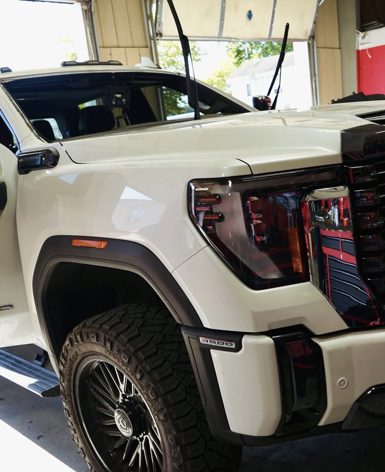Close-up of front left side of a white SUV showing wheel, headlight, and part of the hood.