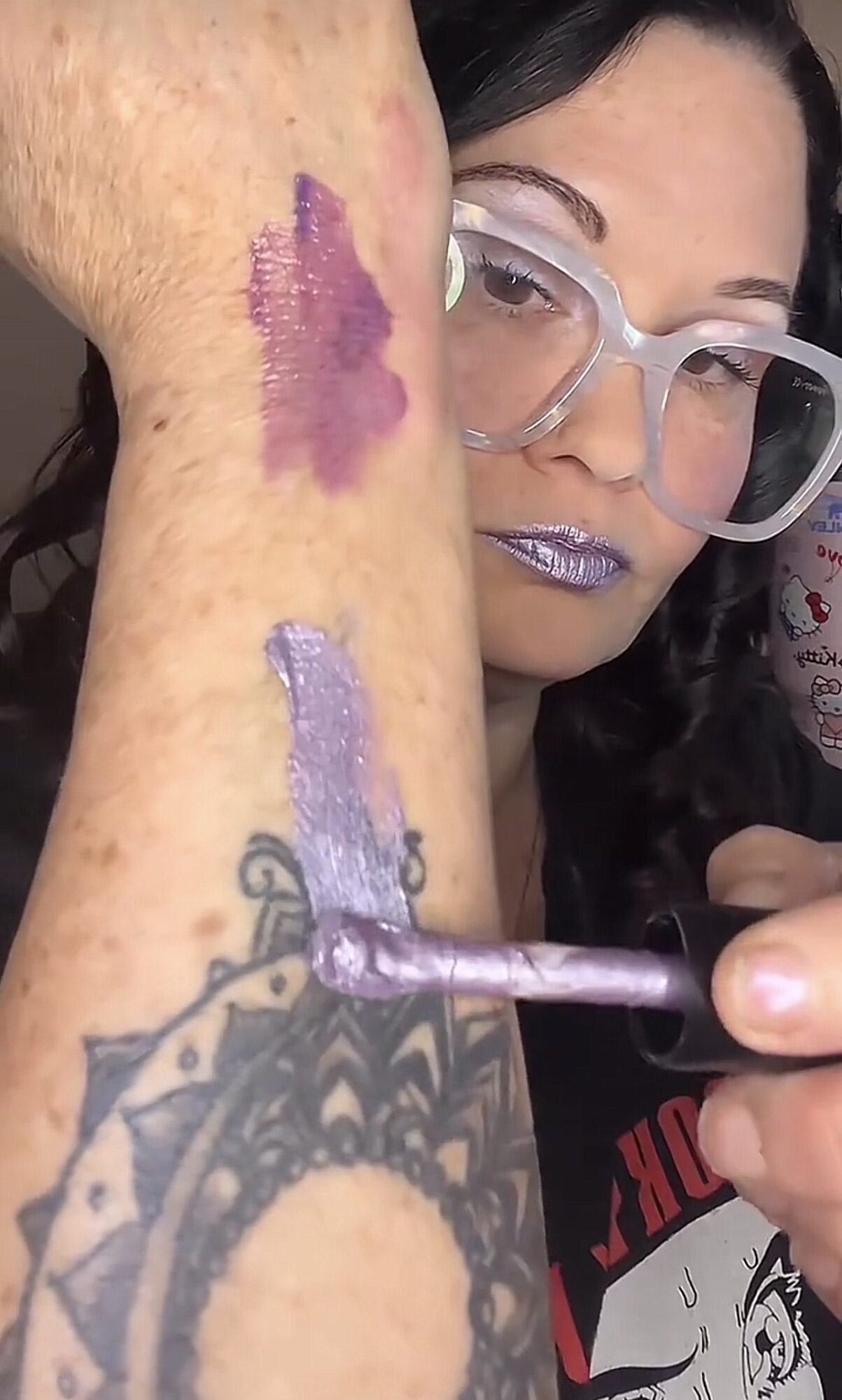 Person with glasses applying purple and lavender tattoo ink to arm with tattoo, close-up view.
