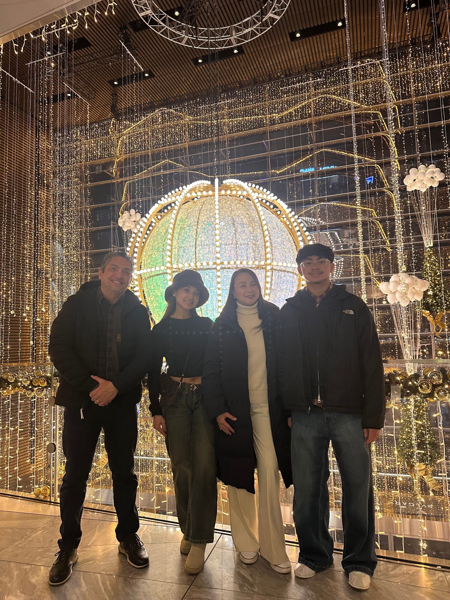 Three people stand in front of a decorated, illuminated structure with a large, circular, glowing centerpiece, at night.
