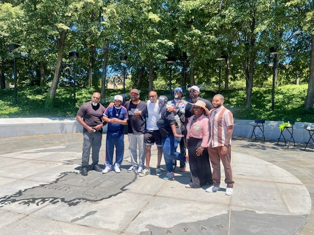 Group of people standing outdoors on a sunny day with trees in the background.