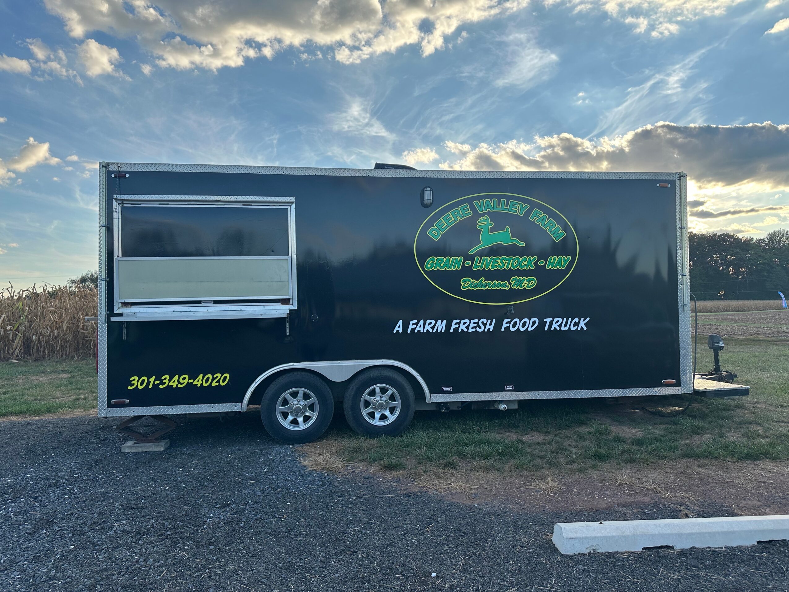 Food truck parked on grass with a blue sky and clouds, logo and contact info visible on side.