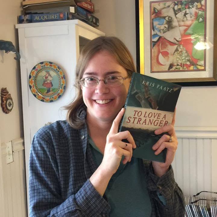 Person with glasses holding a book titled 'To Love a Stranger' in a room with artwork and books.