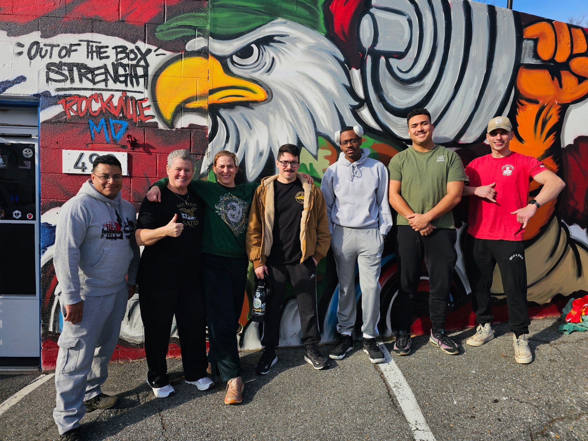 Group of seven people standing in front of a colorful mural of an eagle with a banner reading 'Out of the box strength.'