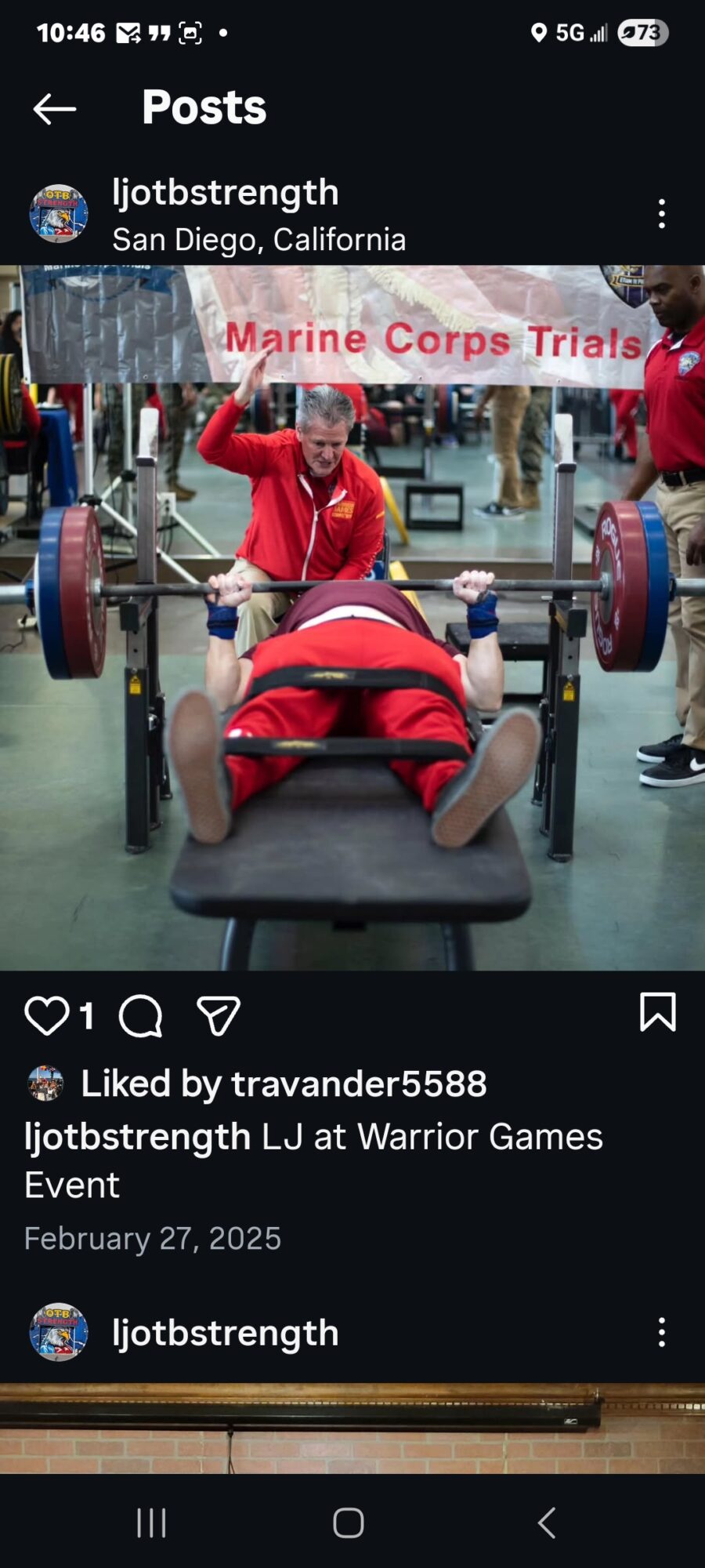 Person in red shirt lying on a bench press with weights, others in red shirts in background, gym setting.