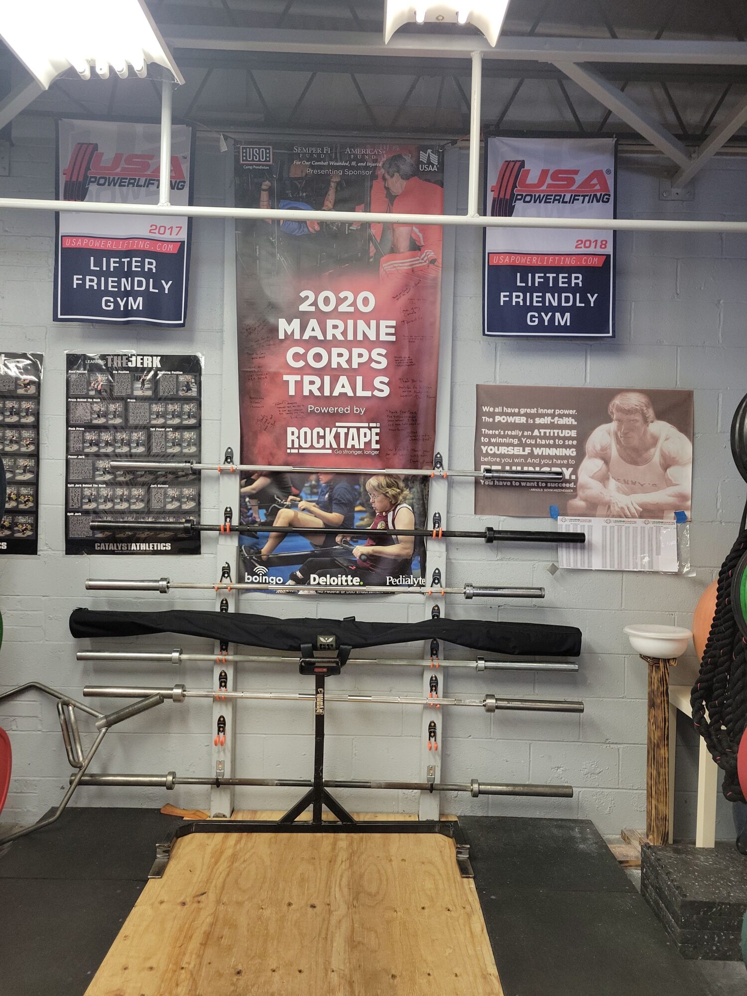 Workout area with a plyometric box, pull-up bars, and posters on the wall, including a 2020 CrossFit competition poster.