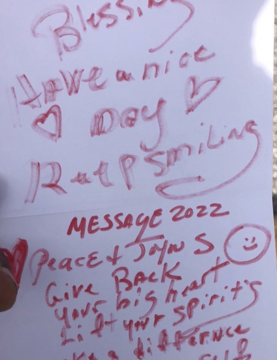 Handwritten note with positive messages and a smiley face, mentioning kindness, smiling, and spirits, on white paper with red ink.
